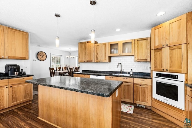 kitchen with white appliances, dark wood-type flooring, sink, pendant lighting, and a kitchen island