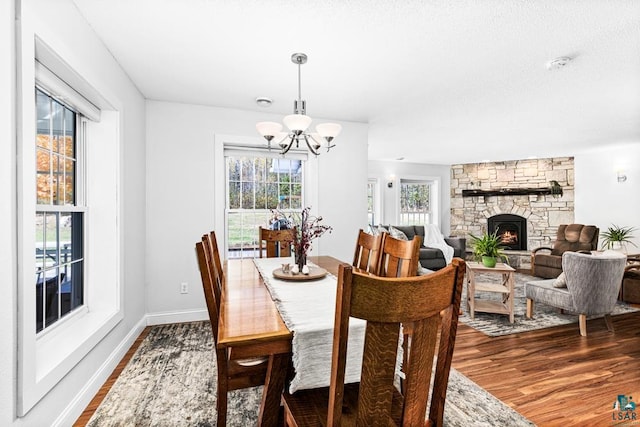 dining area with a stone fireplace, a chandelier, and dark hardwood / wood-style floors