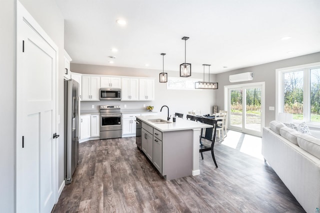 kitchen with decorative light fixtures, a center island with sink, sink, stainless steel appliances, and white cabinetry