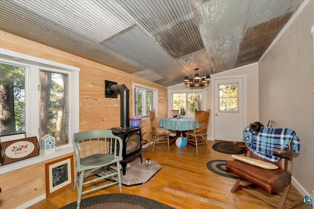 dining area with light hardwood / wood-style flooring, a wood stove, vaulted ceiling, and wooden walls