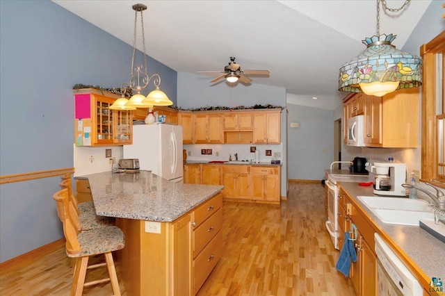 kitchen with white appliances, sink, a kitchen bar, vaulted ceiling, and light hardwood / wood-style flooring