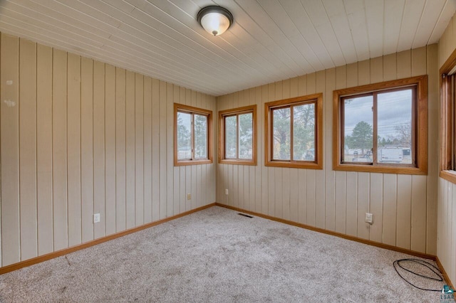 carpeted empty room featuring wood ceiling and wood walls