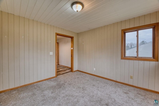 carpeted empty room featuring wood ceiling and wood walls