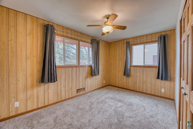 carpeted spare room featuring ceiling fan, a textured ceiling, and wooden walls