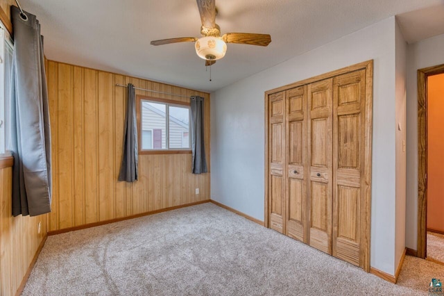 unfurnished bedroom featuring a closet, wood walls, light colored carpet, and ceiling fan