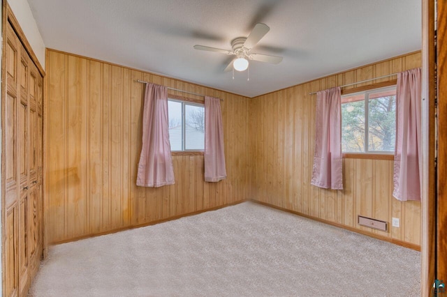 spare room featuring light carpet, wood walls, and a wealth of natural light