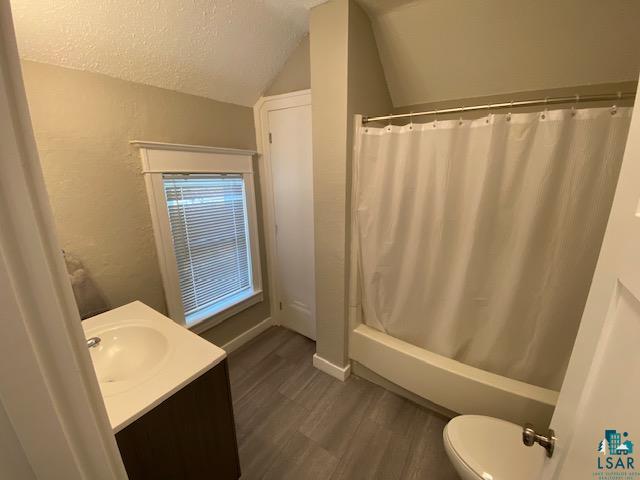 full bathroom with lofted ceiling, toilet, hardwood / wood-style floors, vanity, and a textured ceiling