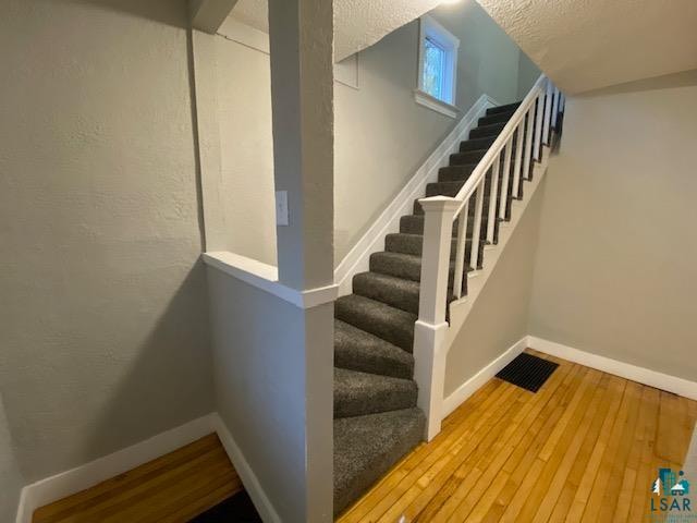 stairs with wood-type flooring and a textured ceiling