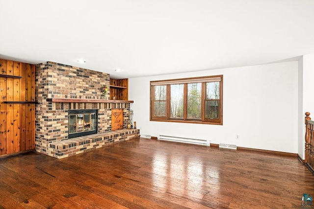 unfurnished living room with baseboard heating, dark hardwood / wood-style flooring, wooden walls, and a fireplace