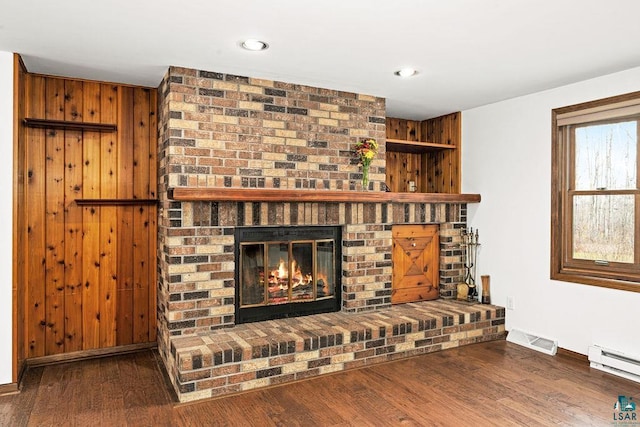 living room with dark hardwood / wood-style floors, baseboard heating, wooden walls, and a brick fireplace