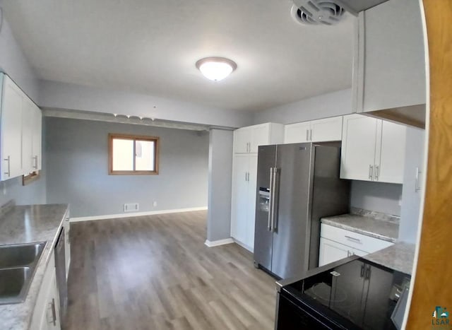 kitchen with black stove, sink, stainless steel fridge, white cabinets, and light hardwood / wood-style floors