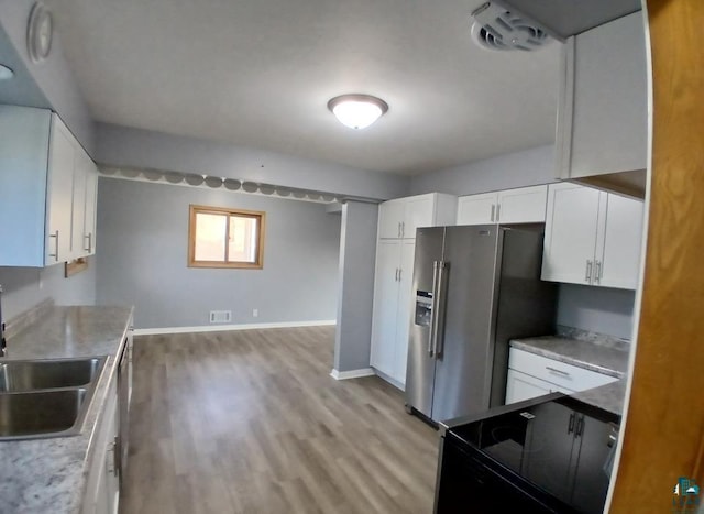 kitchen with white cabinets, stainless steel fridge with ice dispenser, black / electric stove, light hardwood / wood-style floors, and sink