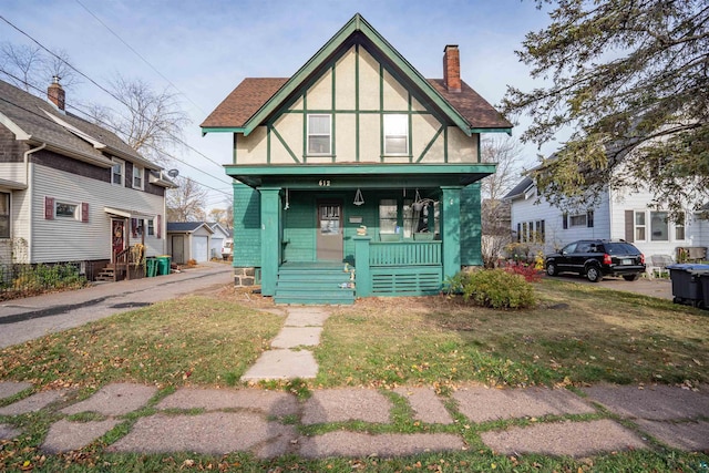 english style home with covered porch and a front lawn