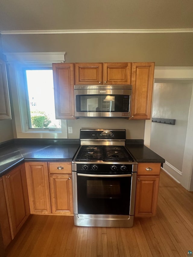 kitchen with crown molding, stainless steel appliances, and light wood-type flooring