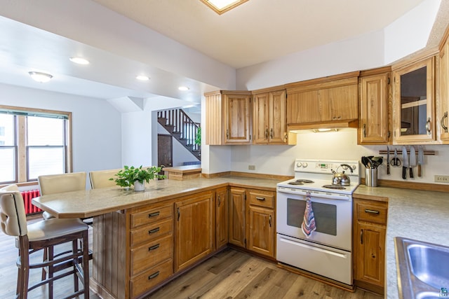 kitchen featuring white electric range oven, kitchen peninsula, sink, a kitchen breakfast bar, and light wood-type flooring