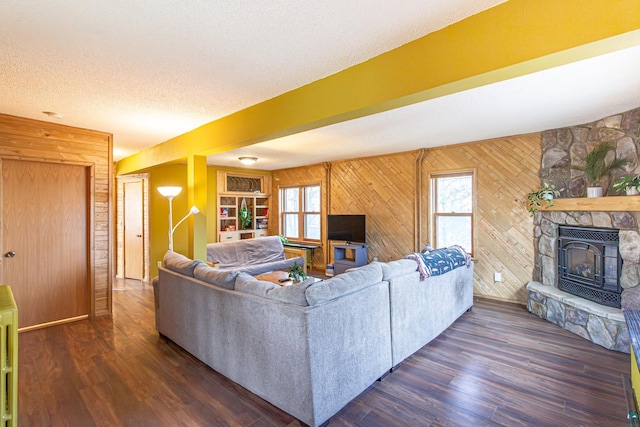 living room with a textured ceiling, a fireplace, dark hardwood / wood-style flooring, and wooden walls