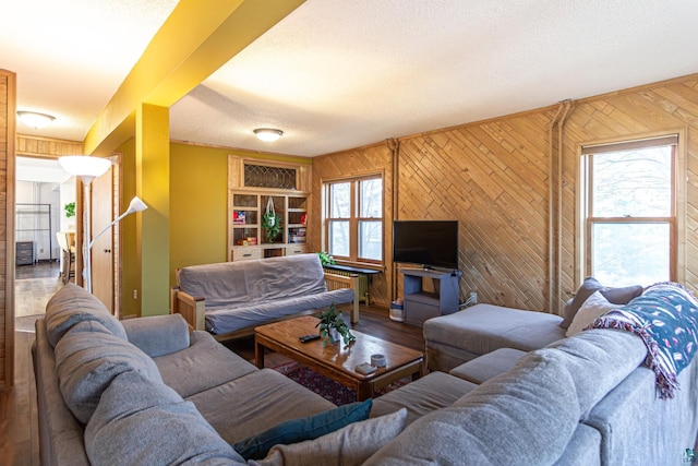 living room with built in shelves, wooden walls, a textured ceiling, and a healthy amount of sunlight