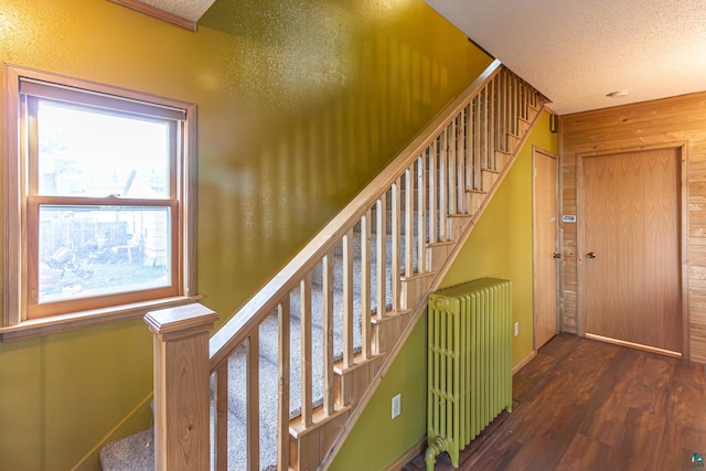 stairway with a textured ceiling, radiator heating unit, wood walls, and hardwood / wood-style flooring