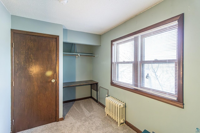 bedroom with a closet, radiator heating unit, a textured ceiling, and light carpet