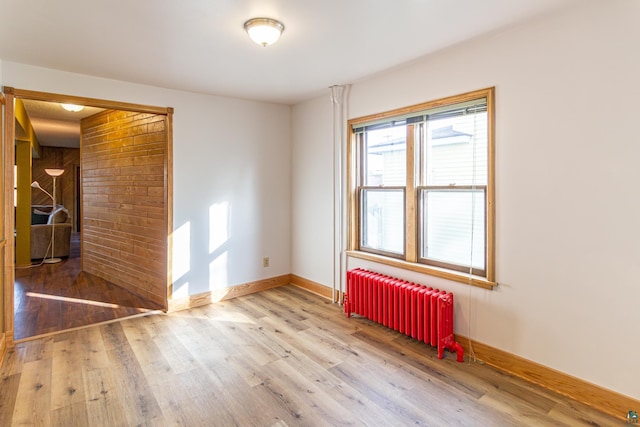 empty room with hardwood / wood-style floors, radiator heating unit, and wood walls