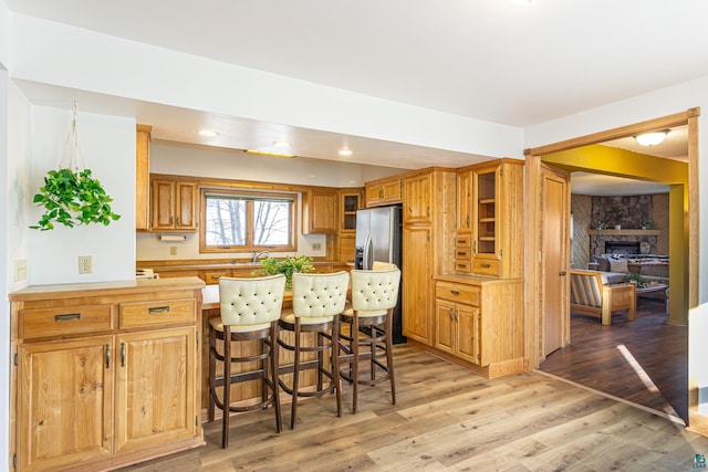 kitchen featuring sink, a kitchen bar, a stone fireplace, light hardwood / wood-style flooring, and stainless steel fridge with ice dispenser