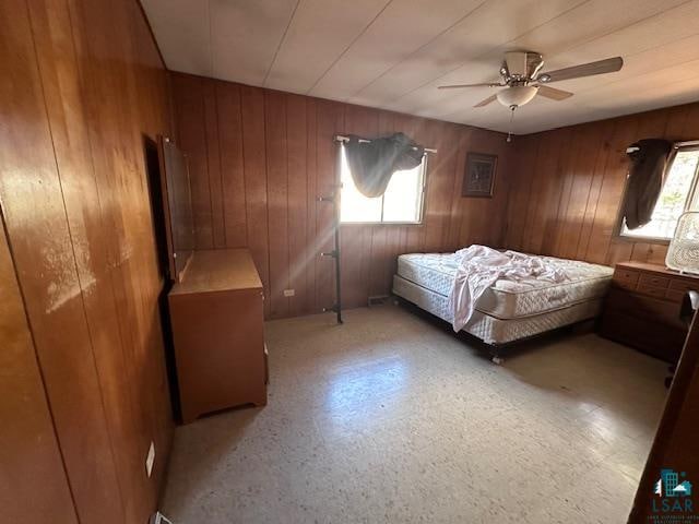 bedroom with wood walls, ceiling fan, and multiple windows