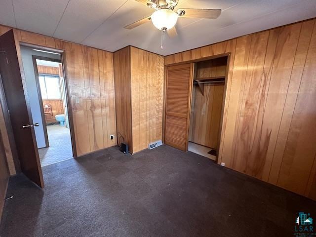 unfurnished bedroom featuring wood walls, ceiling fan, and a closet