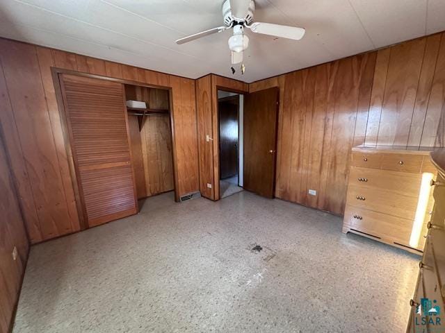 unfurnished bedroom with ceiling fan, wooden walls, and a closet