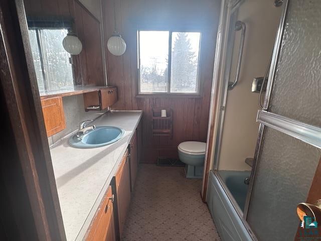 full bathroom featuring combined bath / shower with glass door, vanity, toilet, and wooden walls