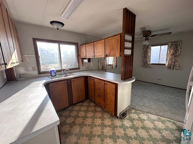 kitchen featuring ceiling fan, sink, kitchen peninsula, and light colored carpet