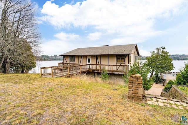 rear view of house with a deck with water view and a yard