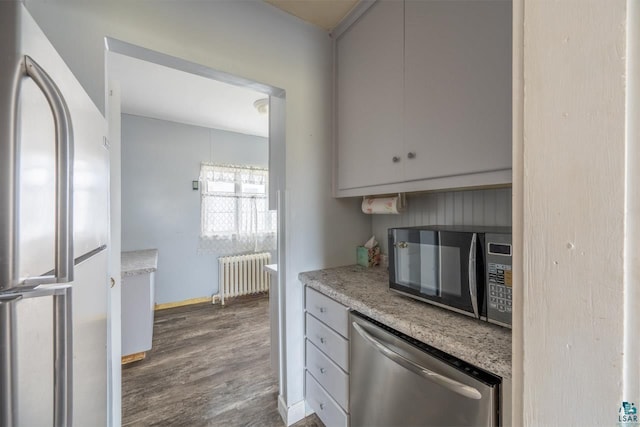 kitchen featuring dark hardwood / wood-style flooring, appliances with stainless steel finishes, and radiator