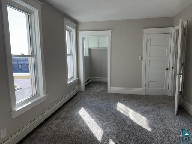 unfurnished bedroom featuring dark colored carpet, baseboard heating, and multiple windows