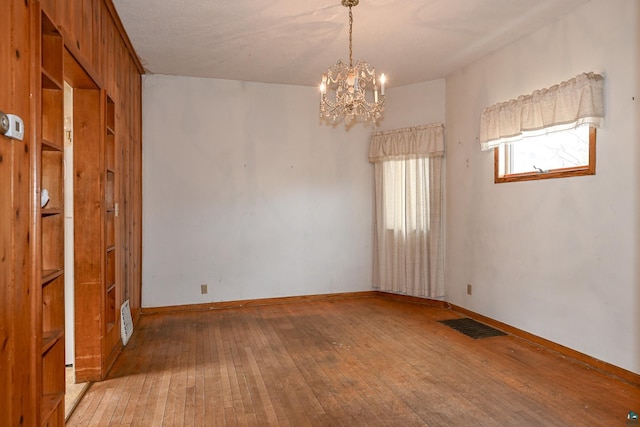 empty room with hardwood / wood-style floors and an inviting chandelier