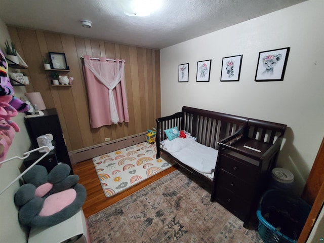 bedroom featuring wood walls, wood-type flooring, and a baseboard radiator