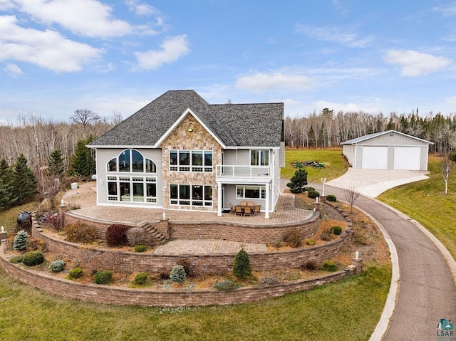 back of house featuring a lawn, a balcony, a garage, a patio area, and an outbuilding