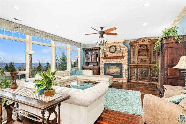 living room with ceiling fan, a fireplace, ornamental molding, and dark wood-type flooring