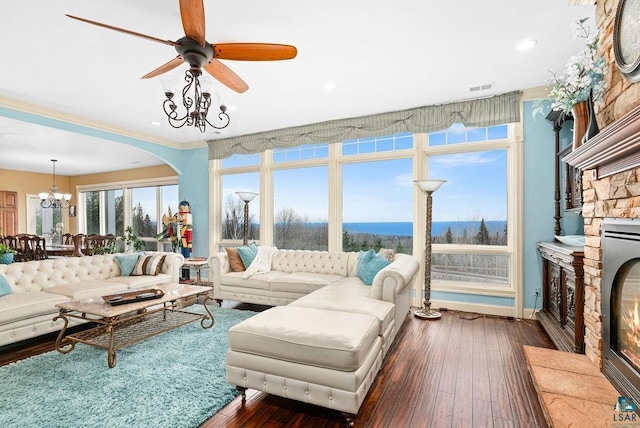 living room with ceiling fan with notable chandelier, dark hardwood / wood-style floors, and a stone fireplace