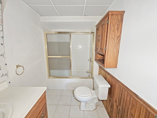 full bathroom featuring tile patterned floors, wood walls, combined bath / shower with glass door, toilet, and vanity