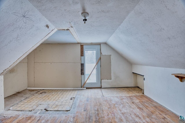 bonus room featuring light wood-type flooring, lofted ceiling, and a textured ceiling