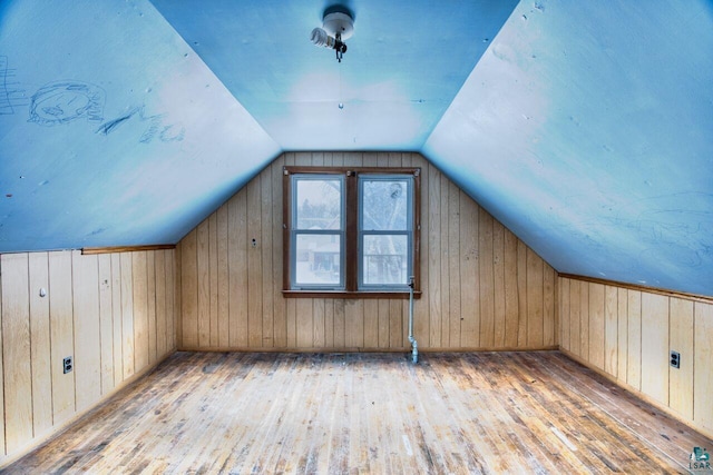 additional living space featuring light hardwood / wood-style floors, vaulted ceiling, and wooden walls