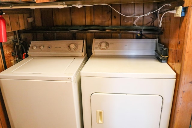 clothes washing area with washing machine and dryer and wood walls