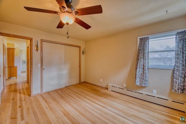 unfurnished bedroom featuring a baseboard heating unit, white refrigerator, ceiling fan, light hardwood / wood-style floors, and a closet