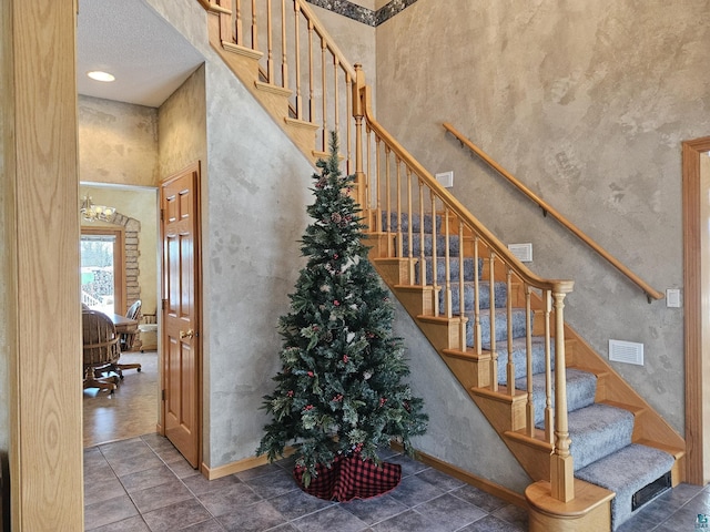 staircase with tile patterned flooring, a towering ceiling, and a textured ceiling