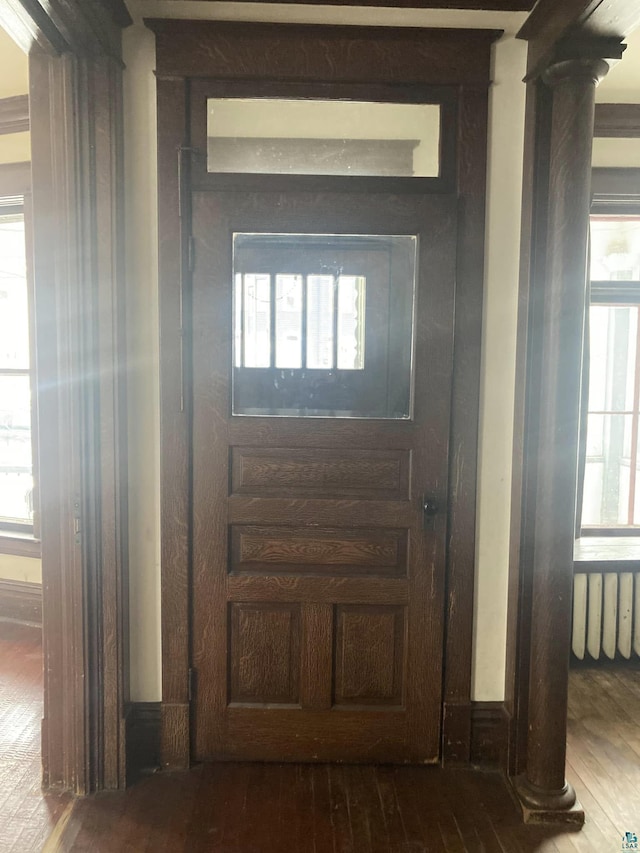 foyer with plenty of natural light, wood-type flooring, radiator, and ornate columns