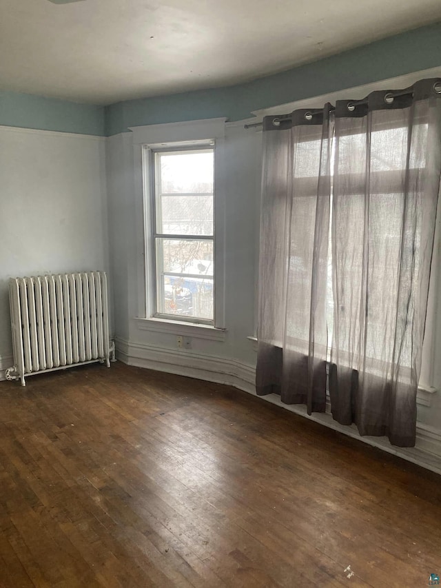 unfurnished room featuring radiator heating unit and dark hardwood / wood-style flooring