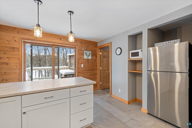 kitchen with white cabinets, stainless steel fridge, wood walls, and pendant lighting