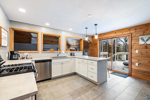 kitchen featuring pendant lighting, dishwasher, white cabinetry, and wooden walls