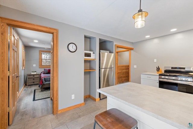 kitchen with a breakfast bar, white cabinets, appliances with stainless steel finishes, decorative light fixtures, and light hardwood / wood-style floors