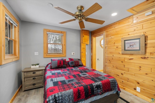 bedroom featuring ceiling fan, wood walls, and light wood-type flooring